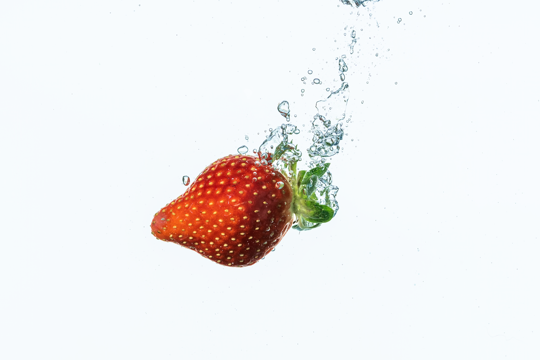 Una fresa vibrante chapoteando en agua con burbujas sobre un fondo blanco.