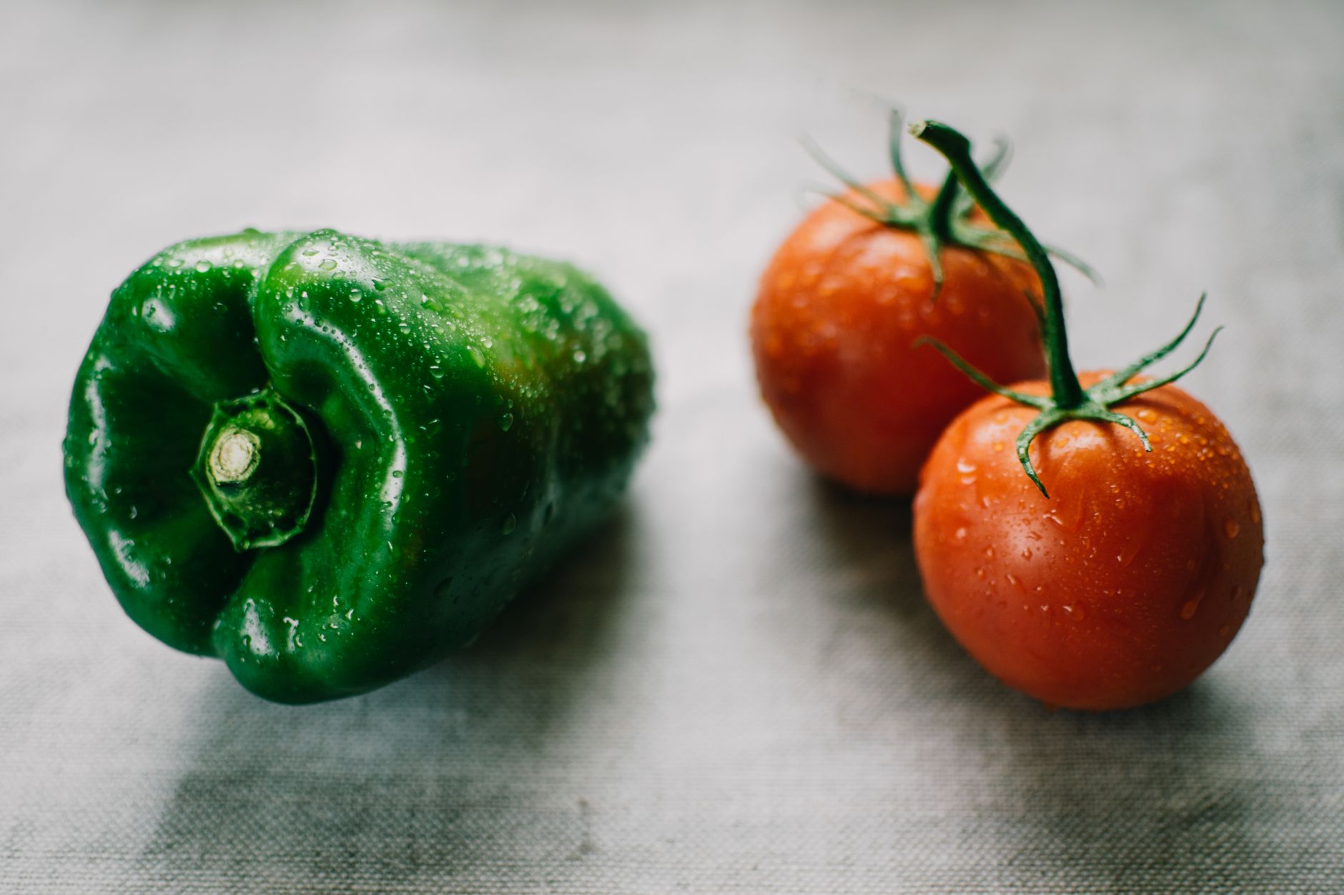 Pimiento verde fresco y tomates con gotas de agua, simbolizando la agricultura orgánica.