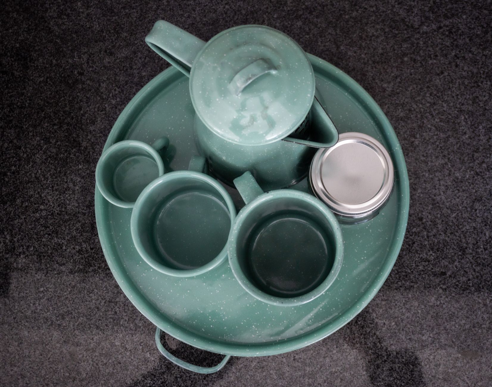Vista superior de un conjunto de tetera de cerámica verde con tazas y un frasco sobre una mesa de piedra.