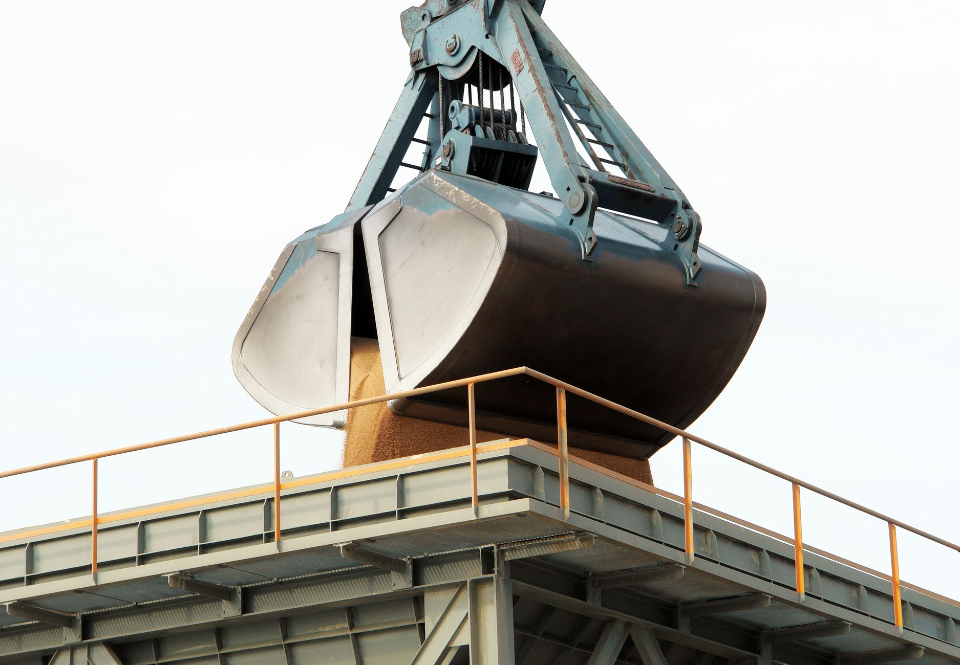 Grúa clamshell descargando carga a granel en un terminal portuario industrial.